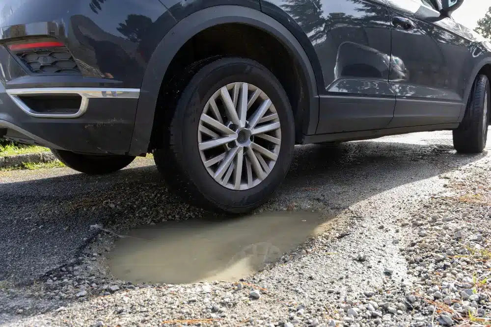 Pothole damage, auto repair in Perryville, MO by Charlie's Tire & Automotive. Image of a vehicle tire dropping into a water-filled pothole on a damaged road. Highlighting ride stability, tire protection, and safe, smooth driving performance.