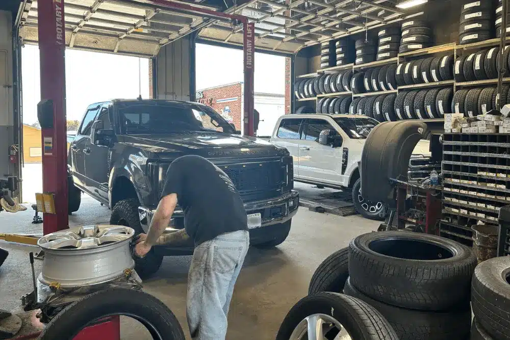Tire care, auto repair in Dexter, MO. An image of a technician performing tire service on a lifted Ford Super Duty truck inside a professional tire and auto repair shop with a large inventory of new tires.