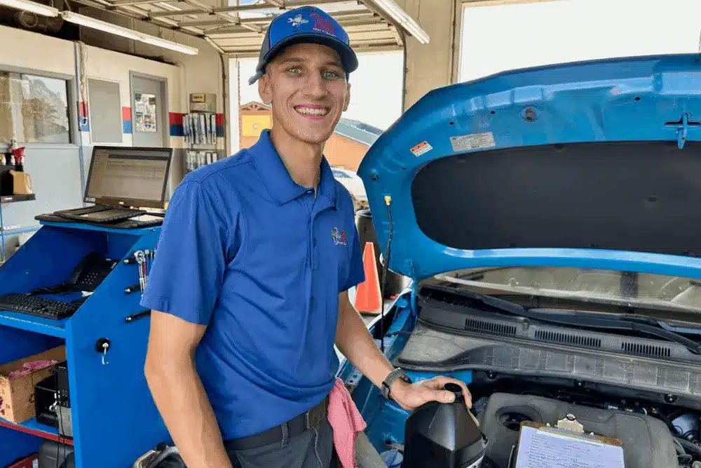 Auto repair mechanic in Peryville, MO, at Charlie's Tire and Automotive. An image of a smiling automotive technician preparing to add fresh engine oil during a professional oil change service with the vehicle hood open inside a modern auto repair shop.