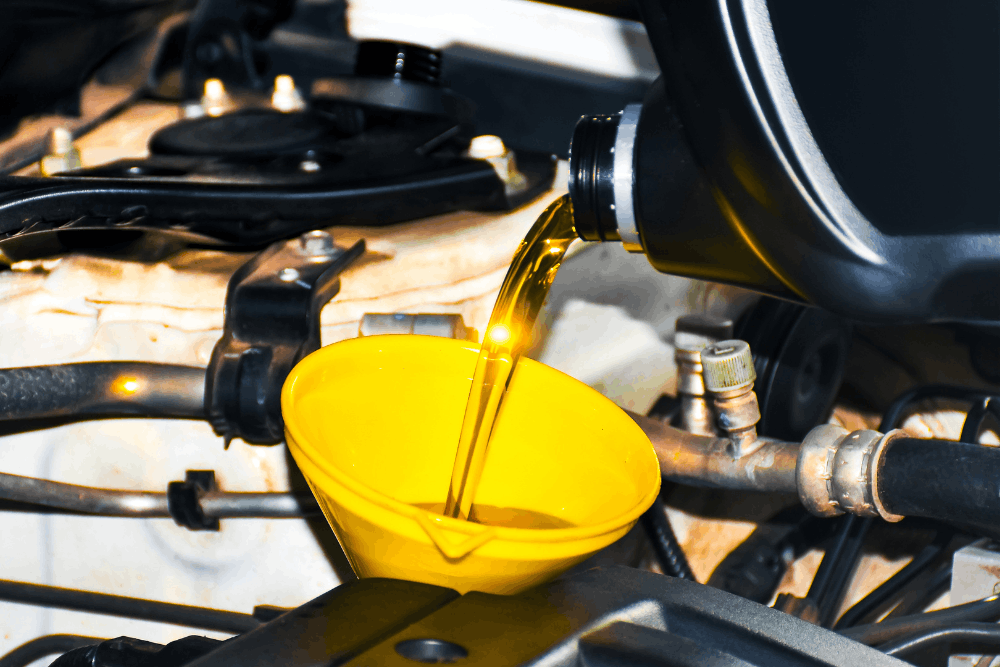 Car care, auto repair in Dexter, MO at Charlie’s Tire and Automotive. Image of fresh motor oil being poured through a yellow funnel into a vehicle engine bay for routine maintenance.